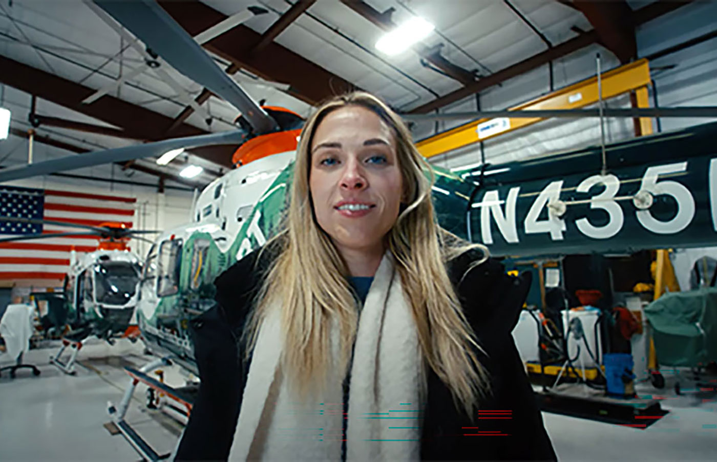 A young woman stands smiling in front of a helicopter ambulance in its hangar.