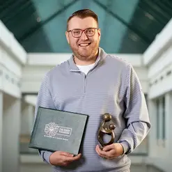 A male health care provider holding a Daisy Award Certificate and Statuette