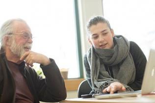 A high school volunteer shows an older adult how to use their computer