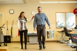 Therapist helps patient walk during therapy session.