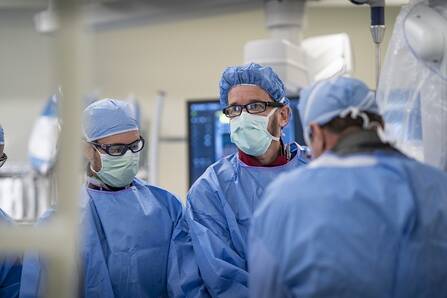 Catheterization lab operating room: 3 gowned providers in a procedure environment