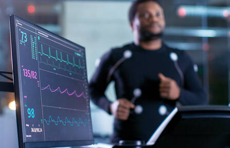 Male athlete runs on a treadmill with a close-up shot of EKG monitor.