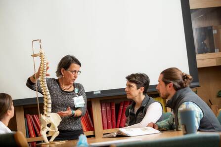 Instructor and 3 students with an anatomical spine  model in classroom