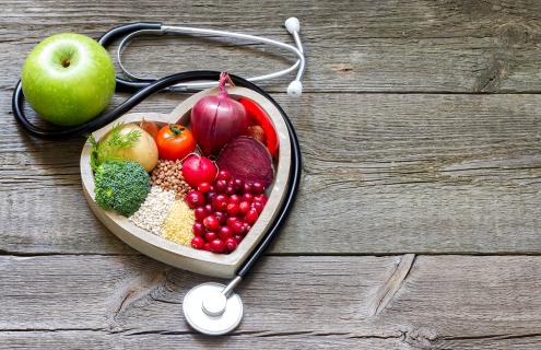 Fruits and vegetables in heart-shaped bowl with stethoscope wrapped around it. 