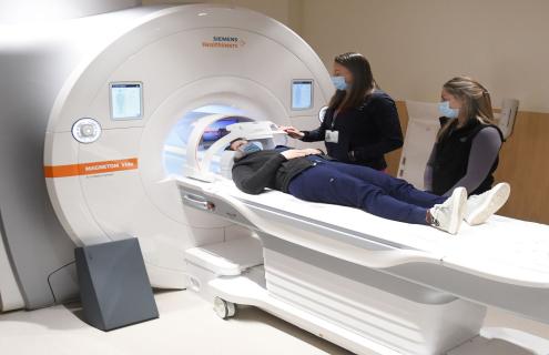 Patient lies on table before entering bore of MRI machine with two healthcare workers at her side