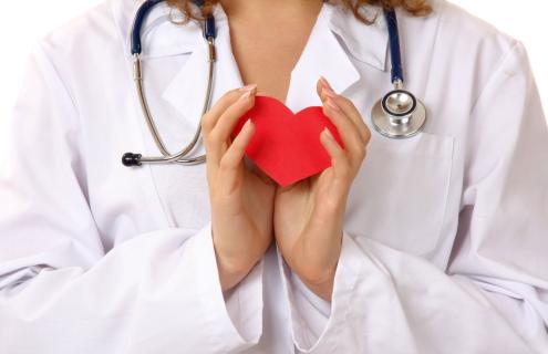 Female physician in white lab coat and stethoscope holding red paper heart
