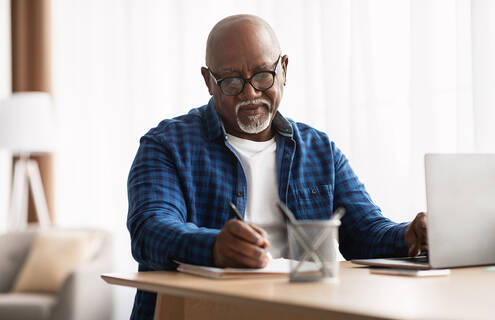 Man looking at a computer and taking notes